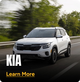White Kia SUV driving fast on a road with tree's in the background. Click to learn more
