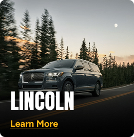 Black Lincoln SUV driving on a road with trees in the background. Click to learn more